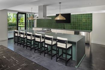 A kitchen with a green tiled backsplash and a long island with chairs.